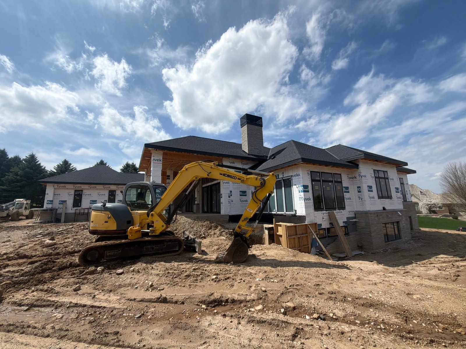 D&D Services excavator doing site work in front of a new custom home under construction